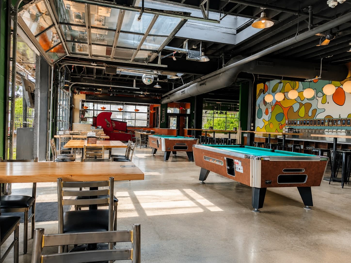 Interior with overhead glass doors open to the patio, exposed structure, polished concrete, pool tables, and a mural